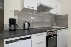 A modern kitchen with a dishwasher, a coffee maker, a kettle, and a stove. - Cozy Studio Near the Wisla River | Balcony | Zabłocie (Kraków)