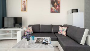 Ein modernes Wohnzimmer mit einem grauen Ecksofa, einem Flachbildfernseher, einem weißen Schrank und zwei gerahmten Kunstwerken an der Wand.