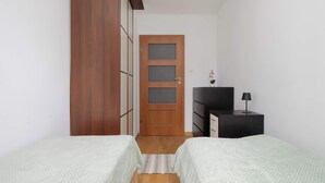 Ein Schlafzimmer mit zwei Betten, einem Kleiderschrank, einem Schminktisch und einer Tür mit satinierten Glasscheiben.