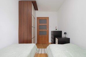 A bedroom with two beds, a wardrobe, a dresser, and a door with frosted glass panels. - Spacious Apartment with Balcony | Workspace | Close to the Center (Warszawa)