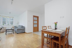 A modern living room with a dining area, wooden furniture, and a view through a large window. - Spacious Apartment with Balcony | Workspace | Close to the Center (Warszawa)