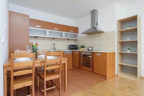 A modern kitchen with wooden cabinets, a dining table set for four, a microwave, oven, and a small plant on the counter. - Spacious Apartment with Balcony | Workspace | Close to the Center (Warszawa)