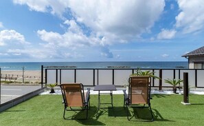 A balcony with two chairs and a table, overlooking a beach and ocean. - Tabinoteitaku Y-beach (yunohama,Tauruoka)