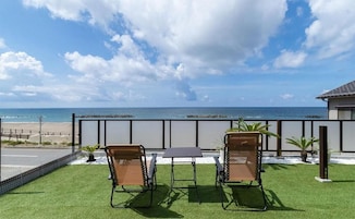 Un balcón con dos sillas y una mesa, con vista a una playa y el océano.