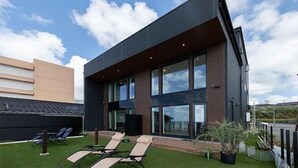 Un edificio moderno con amplios ventanales, techo plano y un pequeño jardín con sillones de relax.