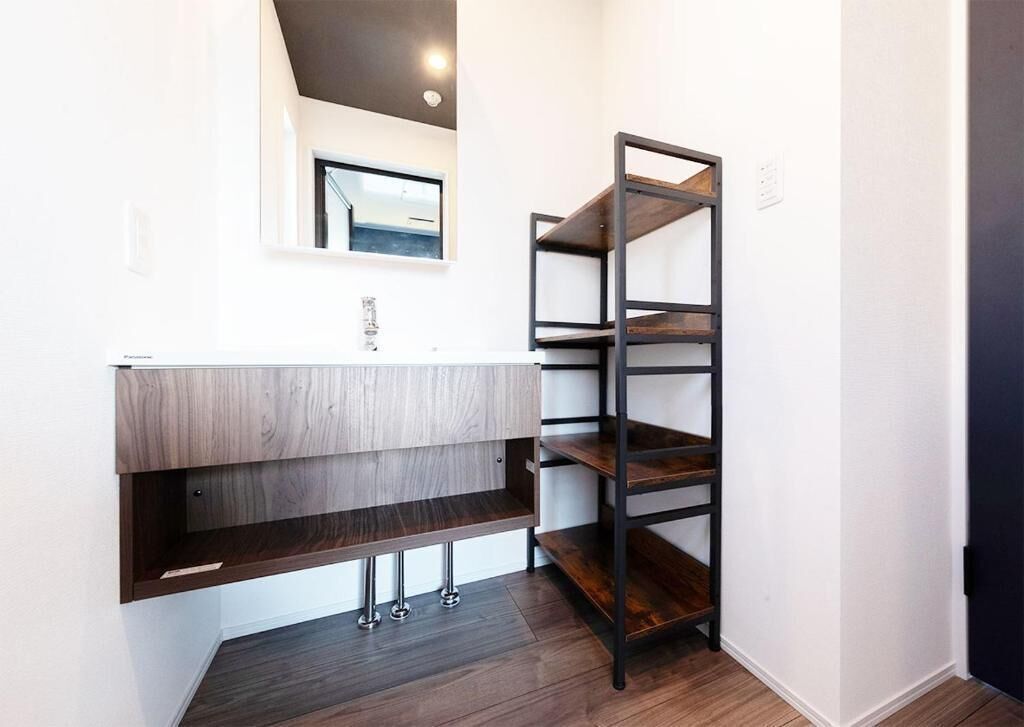 Un baño con tocador de madera, un espejo y una estantería metálica.