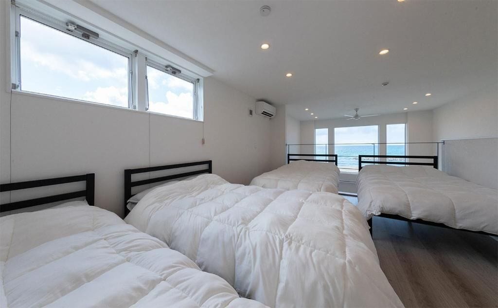 A room with three beds, large windows, and a view of the sea.
