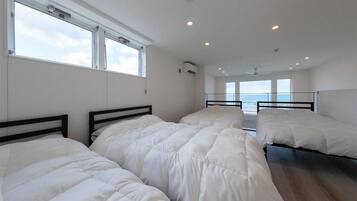A room with three beds, large windows, and a view of the sea.