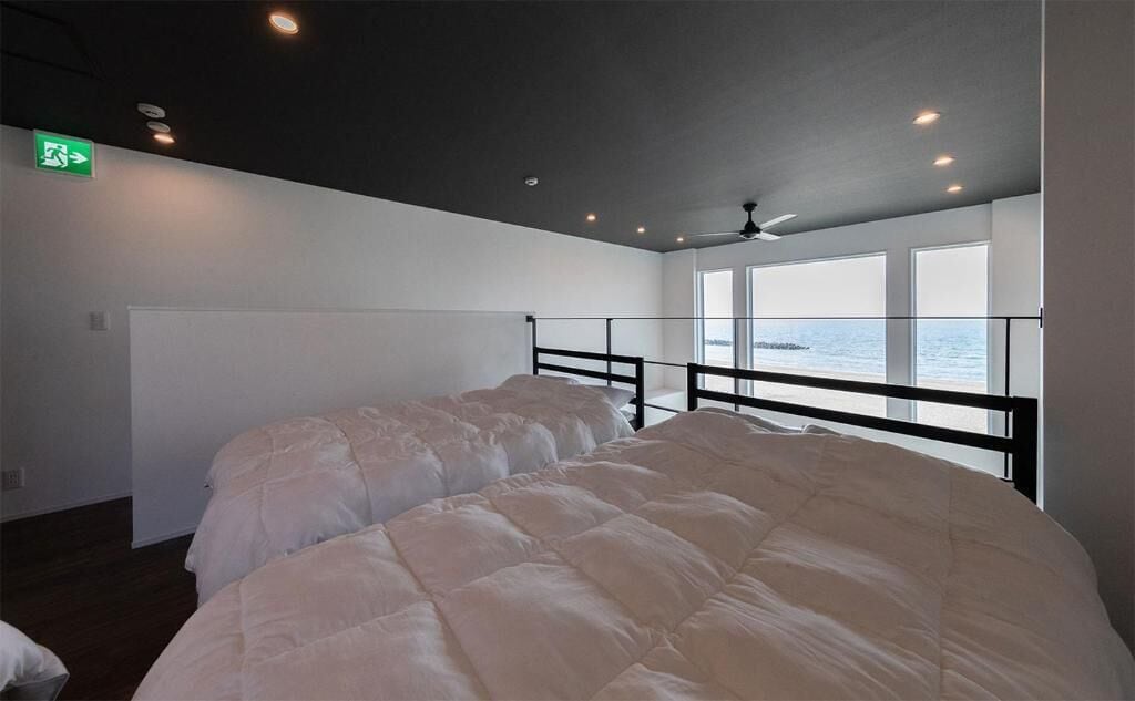 Un dormitorio con una cama, un ventilador de techo y vistas al mar a través de amplios ventanales.