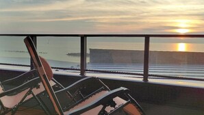 Vista desde un balcón sobre un cuerpo de agua con un atardecer, un edificio grande y una silla.