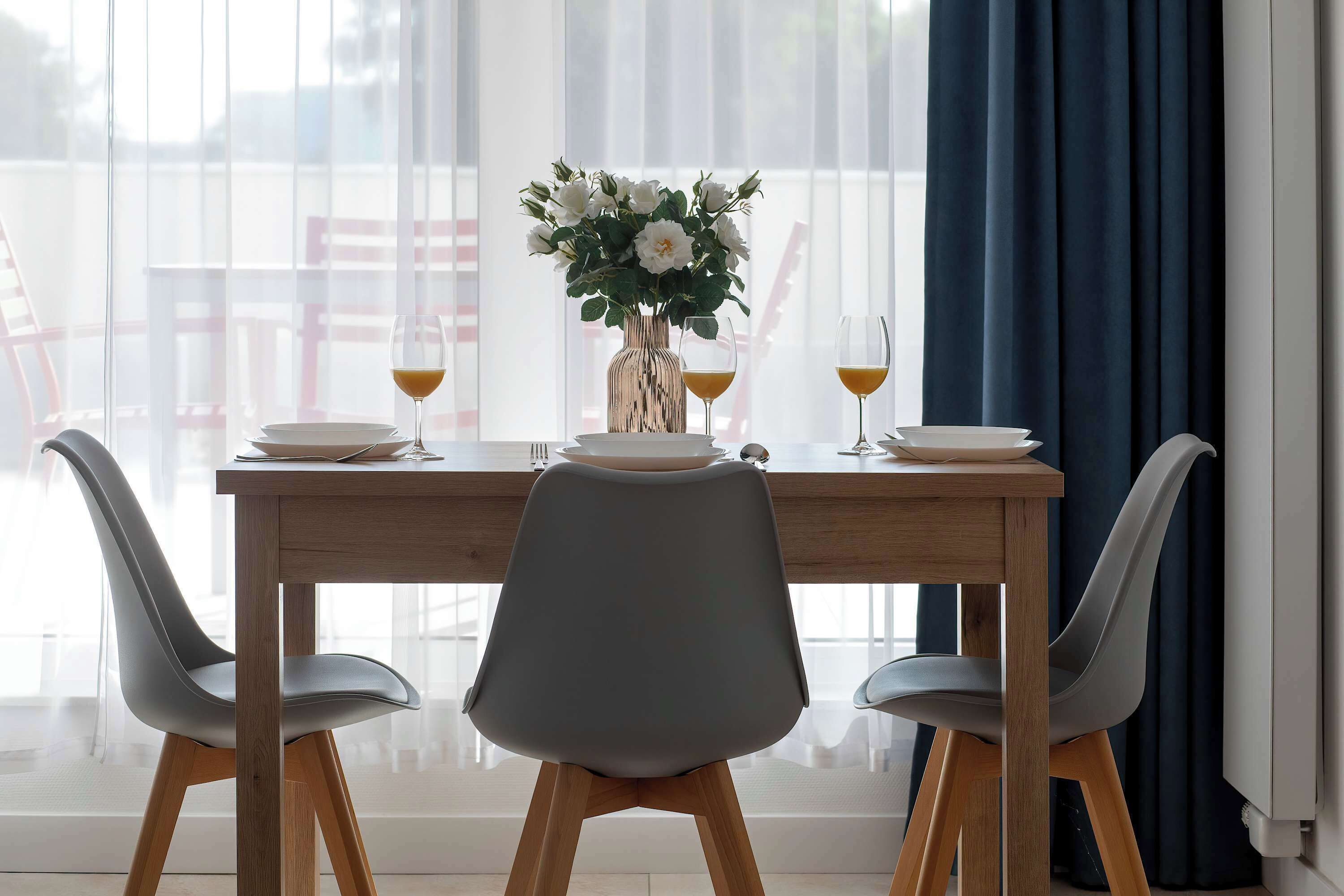Une table à manger dressée pour deux personnes, avec un vase de fleurs, deux verres de jus d’orange et une chaise au design moderne.