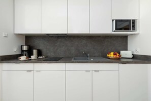 Una cocina moderna con armarios blancos, encimera oscura, cafetera, frutero y microondas.