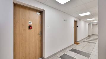 Un couloir avec des portes en bois, des panneaux numérotés et un système d’alarme incendie.
