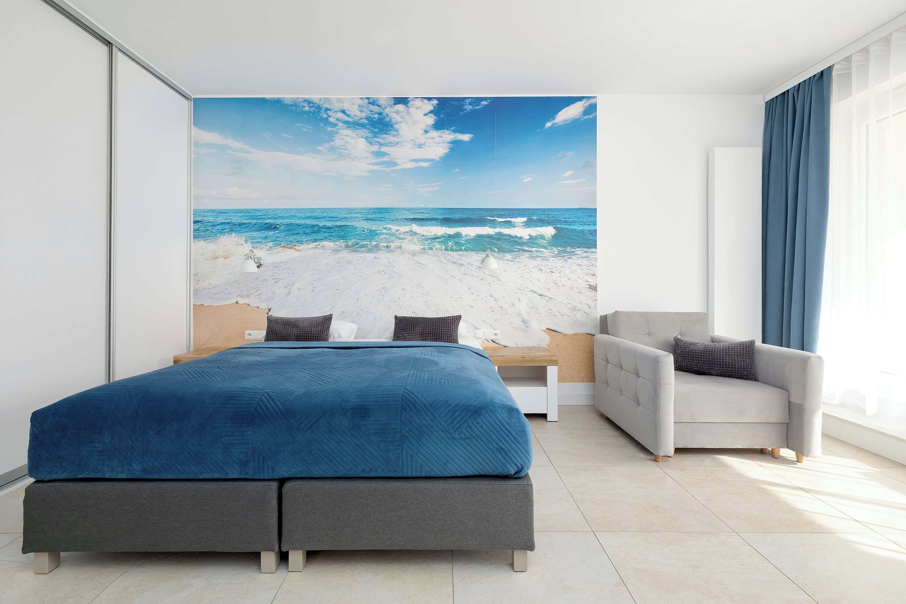 Une chambre avec un lit, une chaise et une fresque murale représentant une plage.
