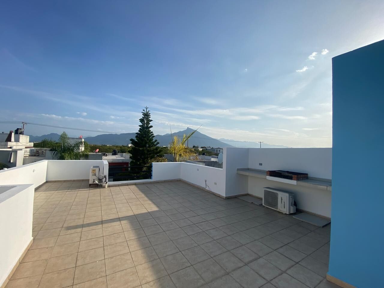 A rooftop terrace with a tiled floor, a small air conditioning unit, and a potted plant.