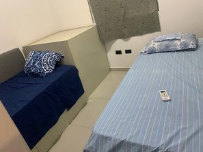 Ein kleines Zimmer mit zwei Betten, eines mit einem gemusterten Kopfkissen und das andere mit einem schlichten.