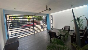Un espace intérieur donnant sur une rue à travers une grille métallique, avec un projecteur fixé au plafond et un coin salon comprenant des chaises et une table.