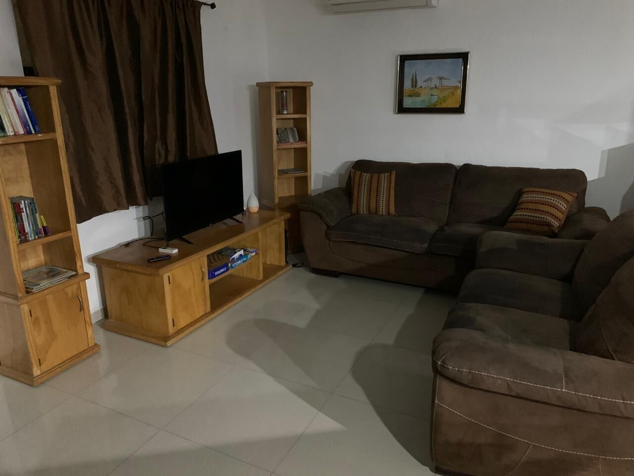 A living room with a sofa set, a TV on a wooden stand, and two bookshelves.