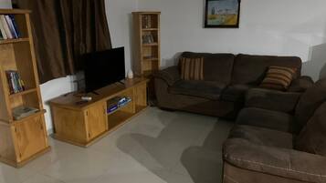 A living room with a sofa set, a TV on a wooden stand, and two bookshelves.
