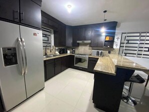 A modern kitchen with stainless steel appliances, dark cabinetry, and a marble countertop.