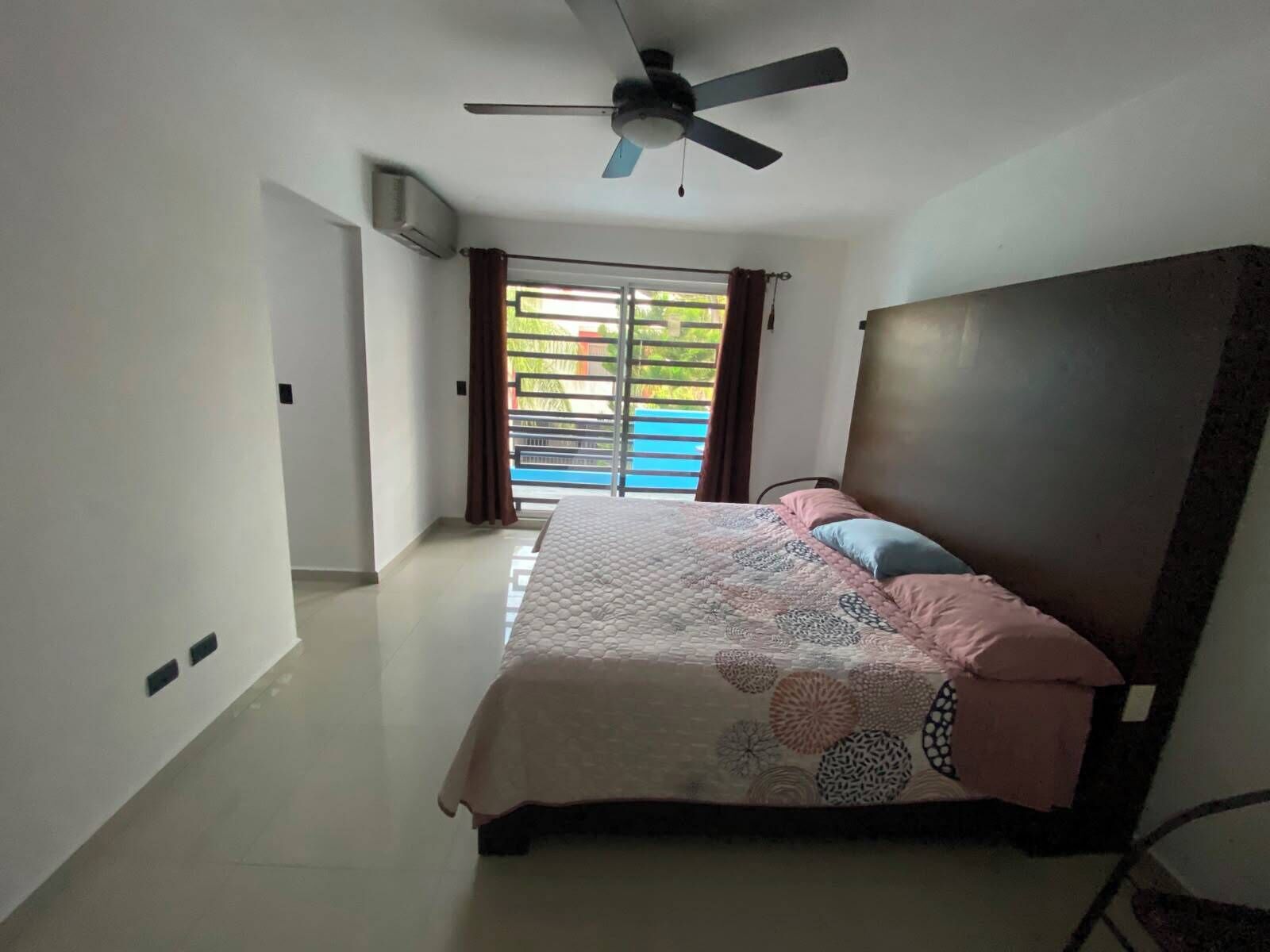 A bedroom with a bed, a ceiling fan, and a view of a pool through a sliding door.