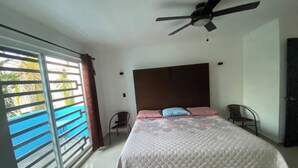 A bedroom with a bed, a ceiling fan, a window with a view, and a chair.
