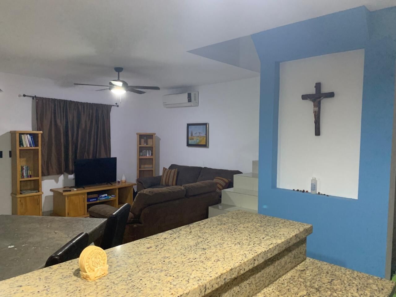 A living room with a television, sofa, and a cross on the wall.