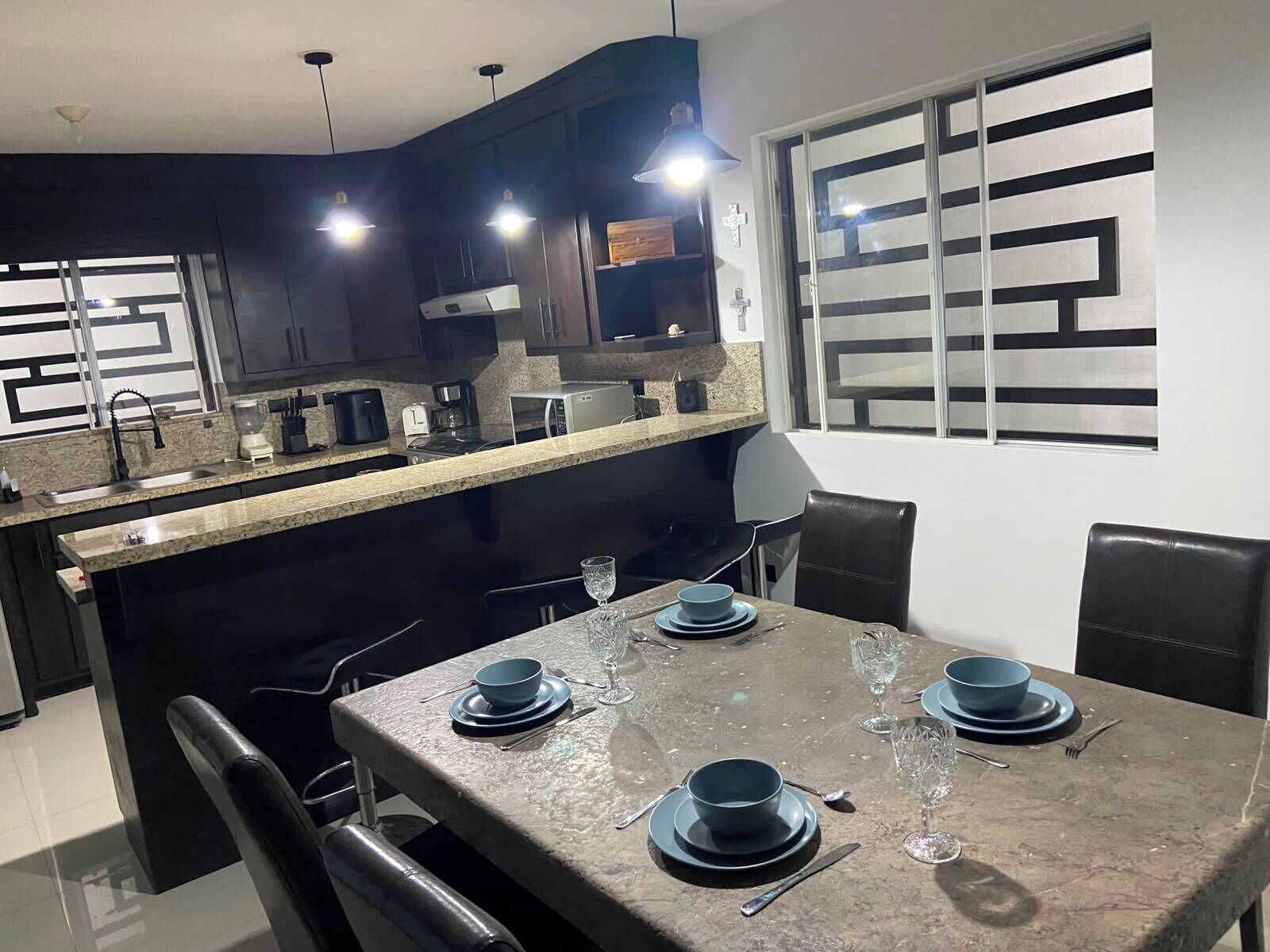 A modern kitchen with dark cabinetry, a granite countertop, and a dining area with a table set for four.