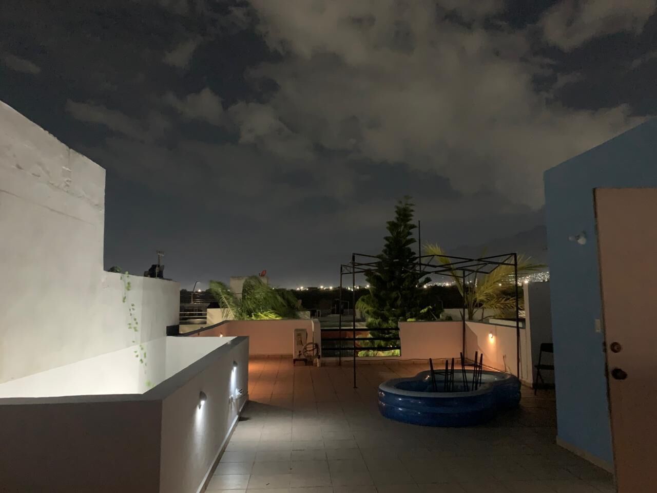 A rooftop terrace with a pool, a white wall, and a metal structure.