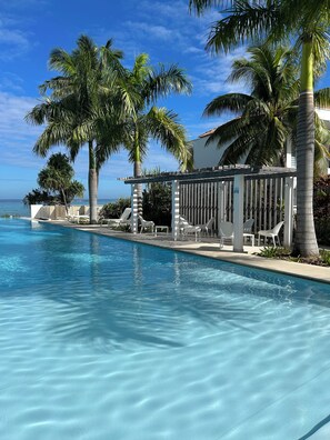 A swimming pool with clear blue water, surrounded by palm trees and white lounge chairs.