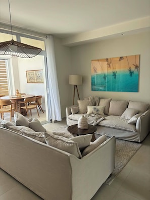 A modern living room with a sofa set, a dining area with a table and chairs, and a large painting on the wall.