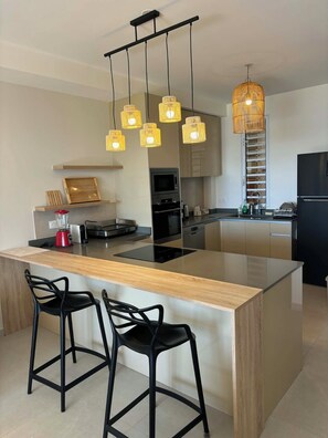A modern kitchen with a central island, bar stools, a built-in oven, and pendant lighting.