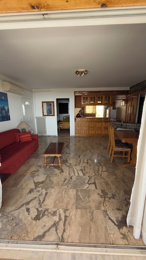 A spacious living area with a red sofa, a wooden coffee table, and a kitchen with wooden cabinets and a tiled backsplash. - Quiet summer / winter house near Athens (Agioi Theodoroi)