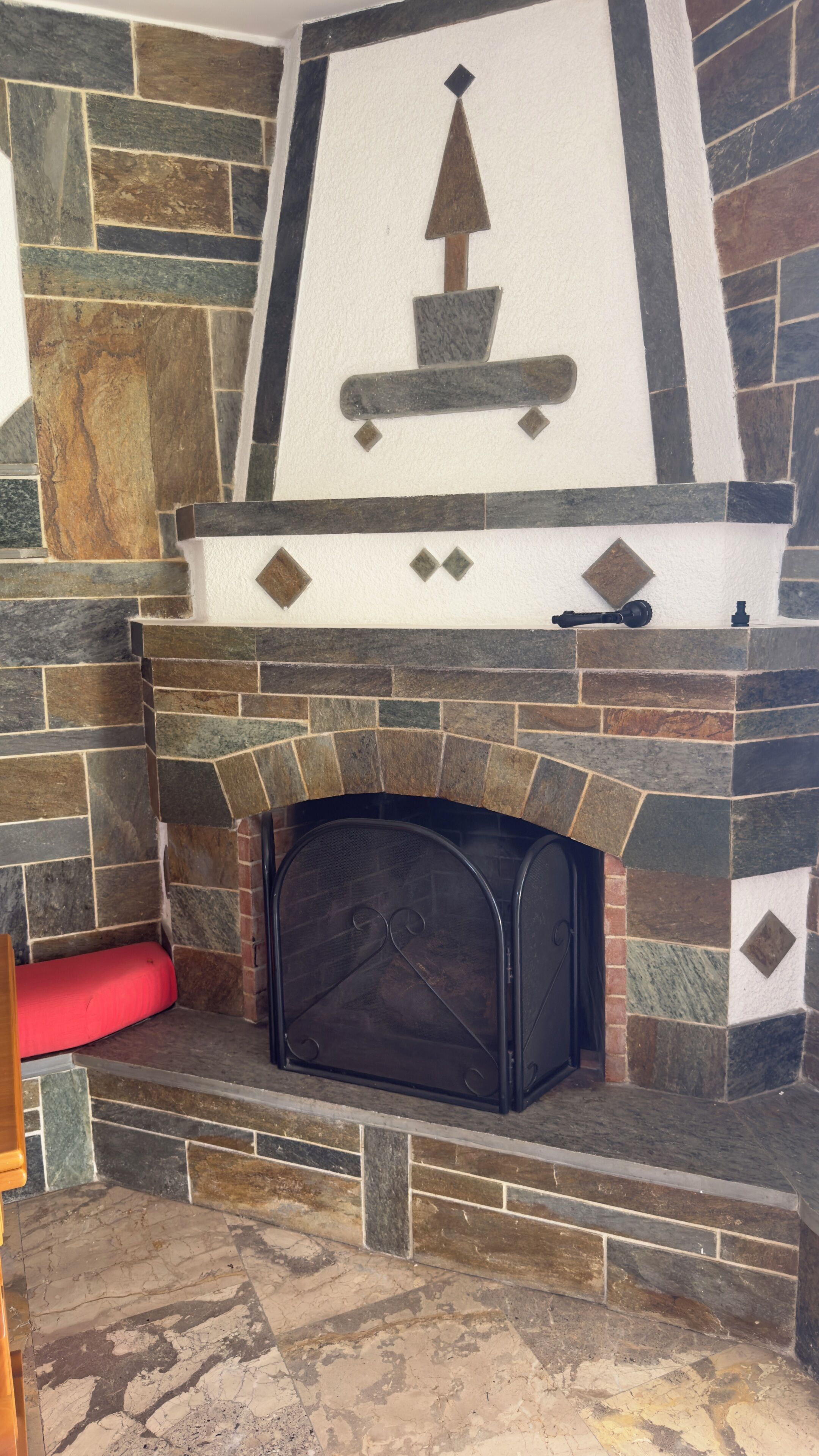 A stone fireplace with a decorative mantelpiece and a red cushion on the left.