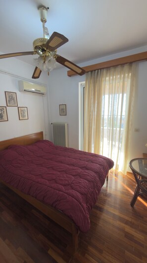 Ein Schlafzimmer mit einem hölzernen Bett, einem Deckenventilator, einer Klimaanlage, einem Heizkörper und einem Fenster mit Vorhängen.