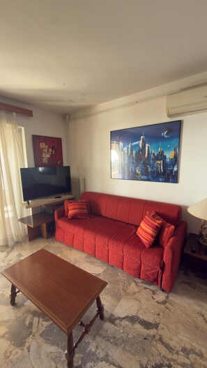 Ein Wohnzimmer mit einem roten Sofa, einem Holztisch, einem Flachbildfernseher und einem Stadtbild an der Wand.