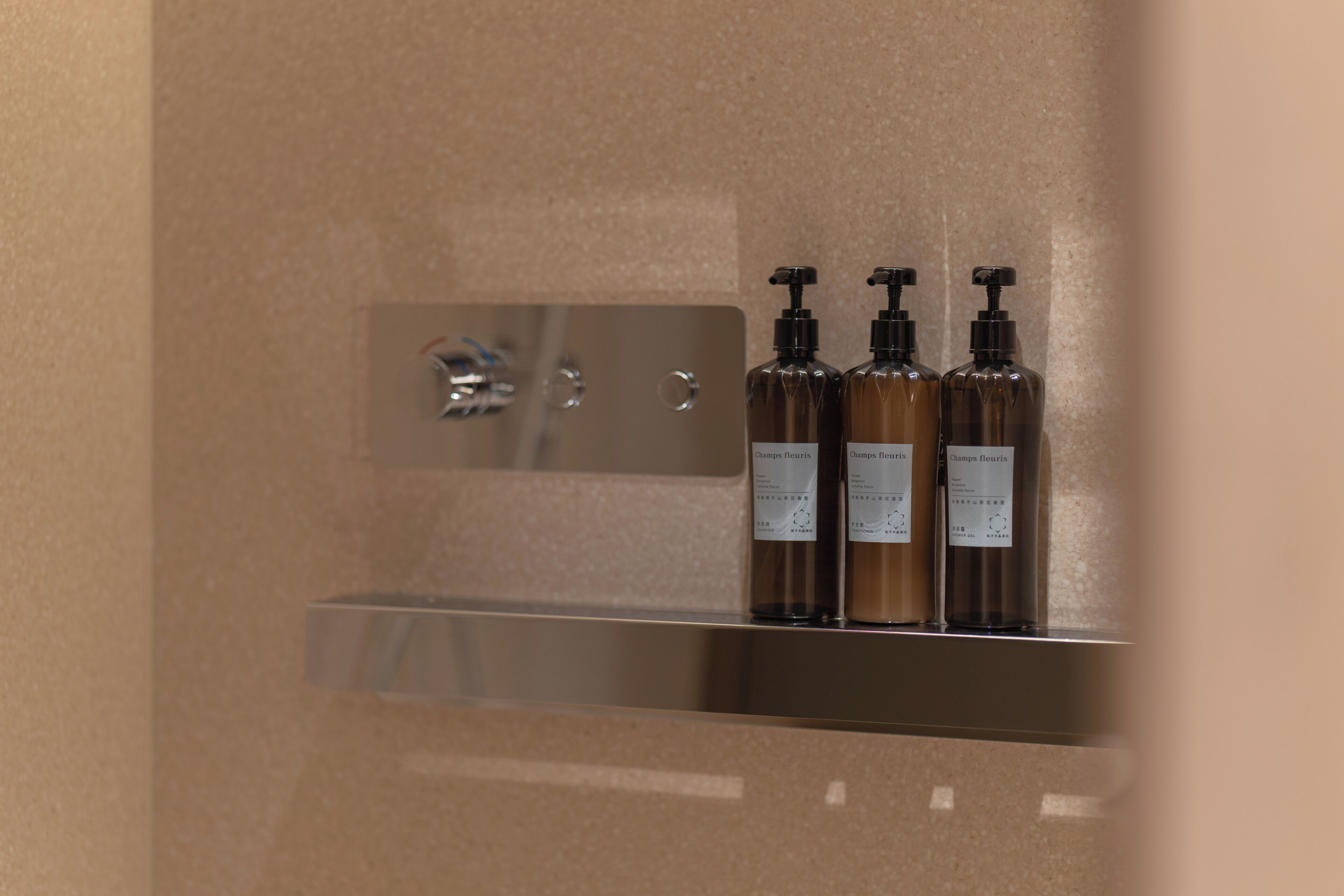 A bathroom with a chrome sink and three bottles of shampoo on a shelf.