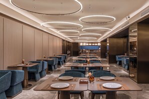 Un ristorante moderno con diversi tavoli, sedie imbottite blu e una passerella centrale.