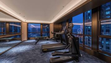 A gym with treadmills and exercise equipment, large windows with city views, and a carpeted floor.