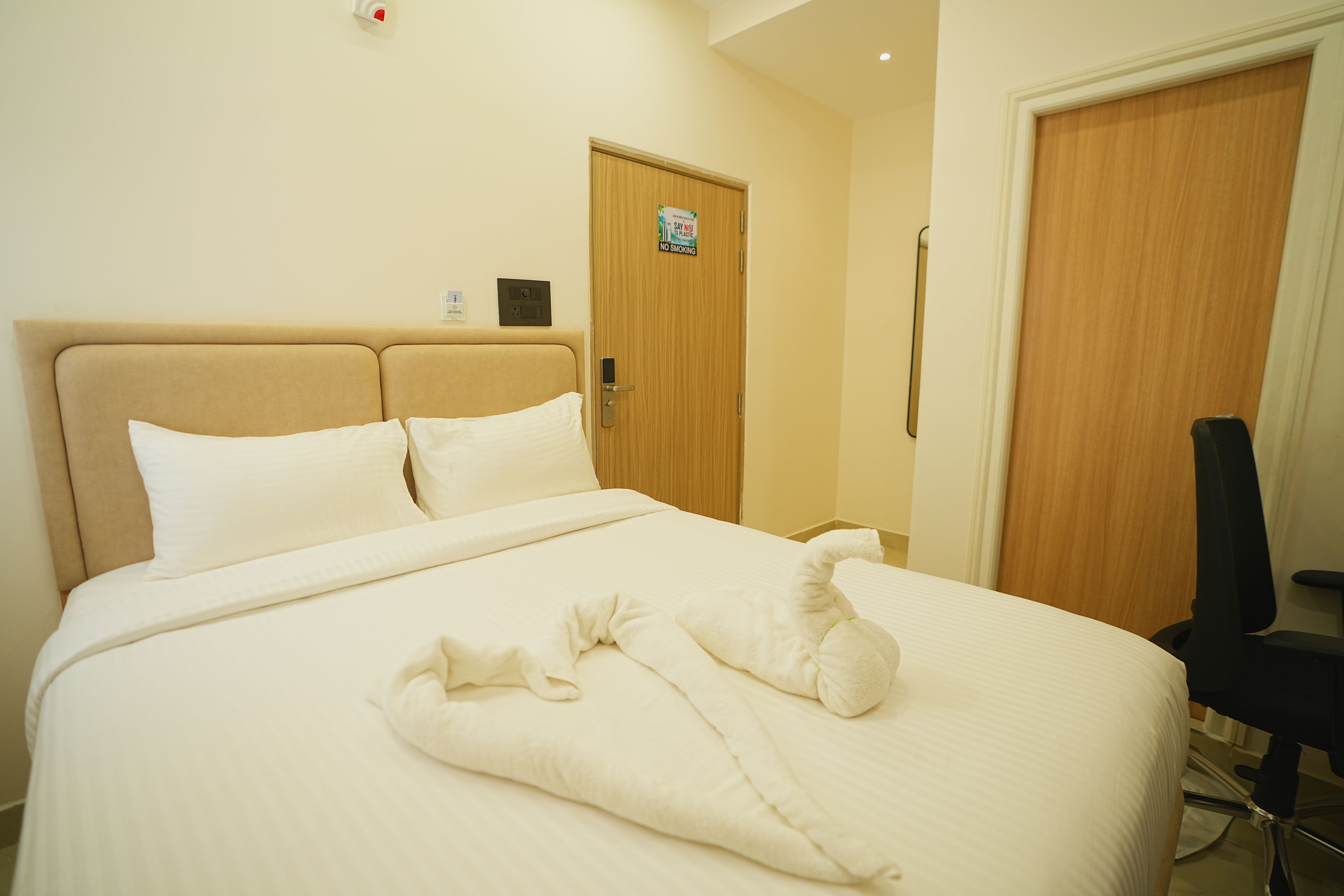 Habitación de hotel con cama, bata, silla y puerta con un cartel de 'No Fumar'.