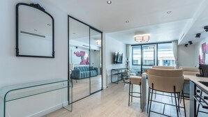 En modern inredning med en glasvägg, en blå soffa, en matplats med barstolar och ett kök.