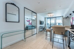A modern interior with a glass partition, a blue sofa, a dining area with bar stools, and a kitchen. - Renovated 1BR | Steps from Croisette & Beach (Cannes)