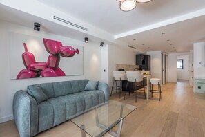 A modern living room with a grey sofa, a glass coffee table, and a vibrant abstract painting on the wall. - Renovated 1BR | Steps from Croisette & Beach (Cannes)