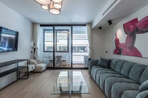 A modern living room with a grey sofa, a glass coffee table, and a flat-screen TV mounted on the wall. - Renovated 1BR | Steps from Croisette & Beach (Cannes)