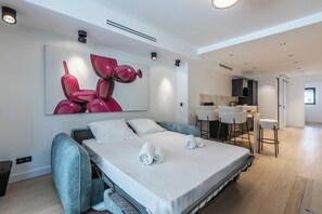 A modern hotel room with a large bed, a dining area, and a kitchen. - Renovated 1BR | Steps from Croisette & Beach (Cannes)