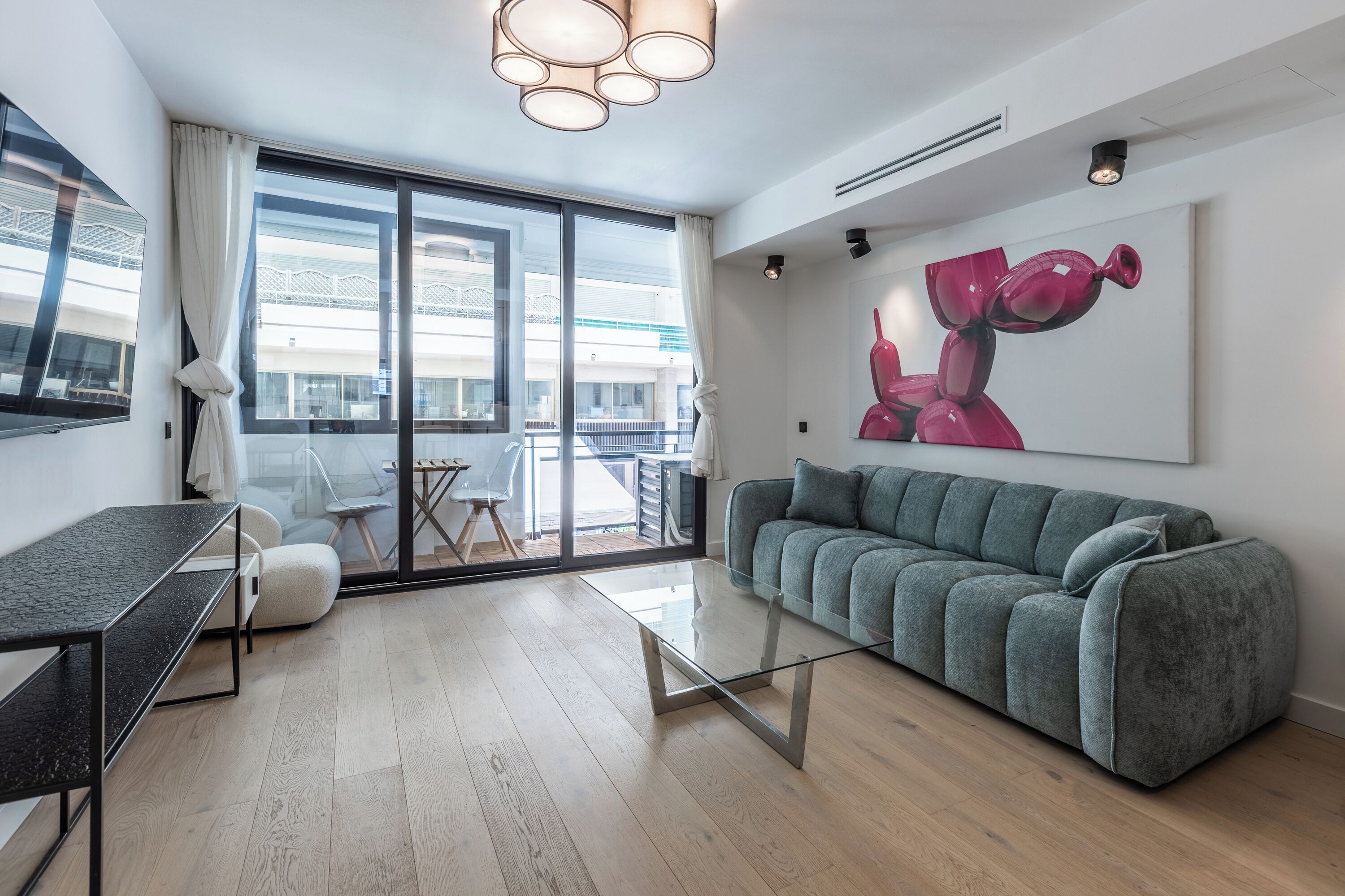 A modern living room with a grey sofa, a glass coffee table, and a dining area with a table and chairs.