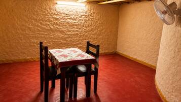 A small room with a table and chairs, a fan, and a textured wall.