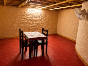 A small room with a table and chairs, a fan, and a textured wall. - Sariska Tiger Lodge (Rajgarh)
