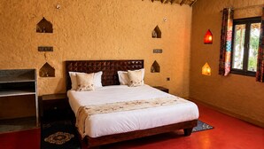Una habitación con una cama, cabecera de madera, piso rojo y una ventana con cortinas.