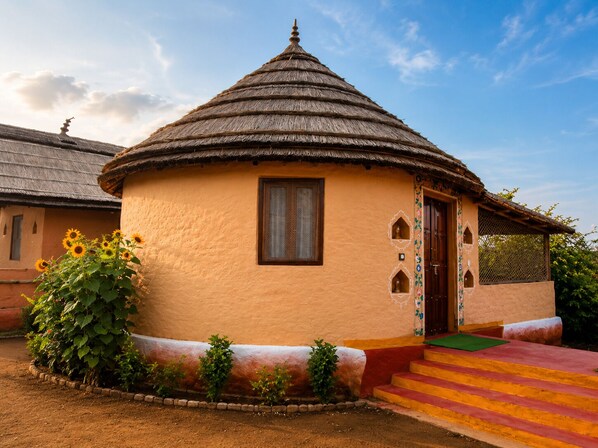 A traditional round hut with a thatched roof, a small window, and a door with decorative elements. - Sariska Tiger Lodge (Rajgarh)
